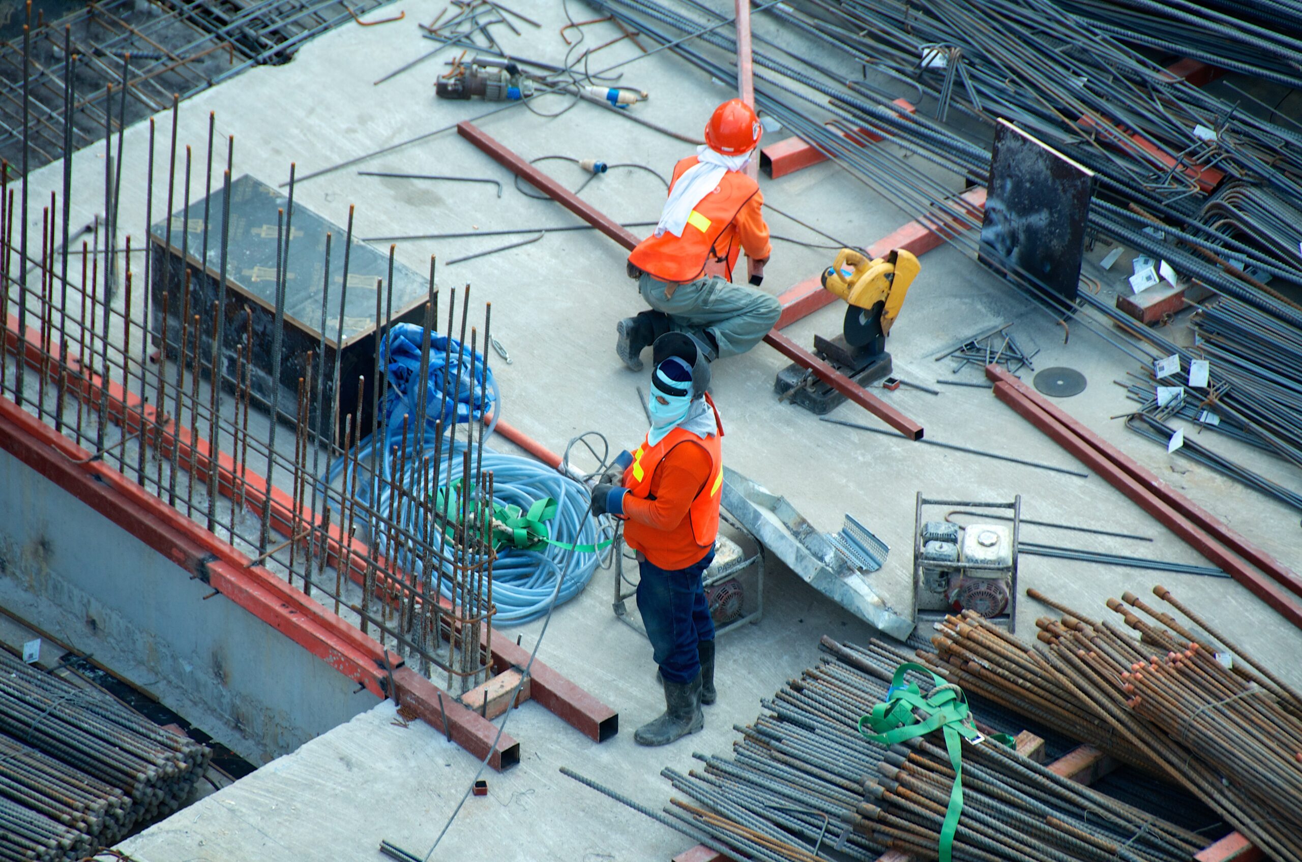 Construction worker standing on a concrete surface surrounded by metal poles and another construction worker
