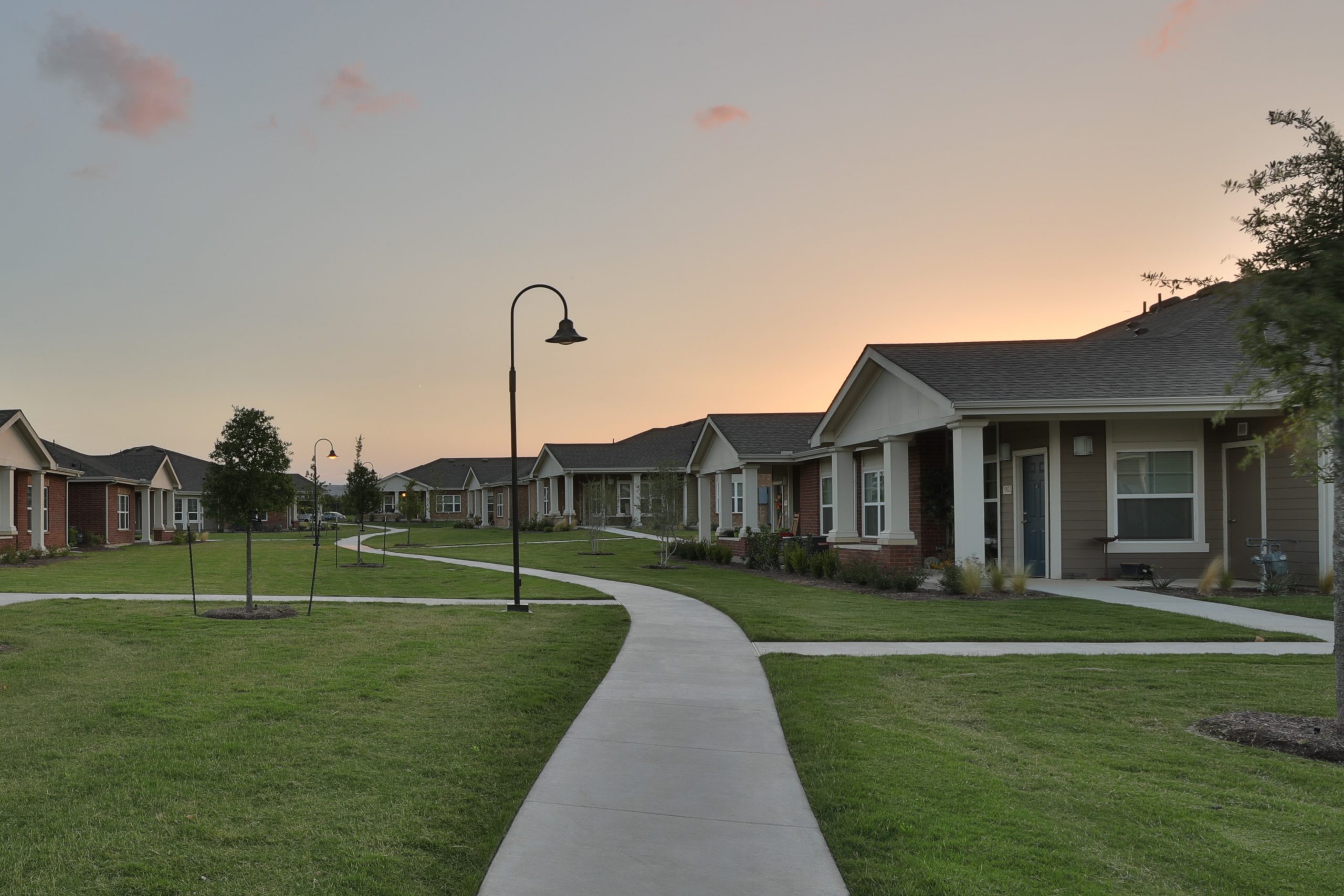 Sidewalk going through housing community with grassy lawns and a sunset sky