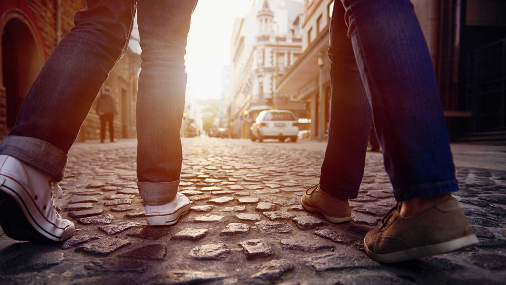 Close up of two pairs of feet in tennis shoes walking on a cobblestone road